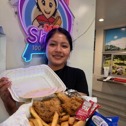 Una clienta con pollo frito y papas junto al rótulo de neón adentro