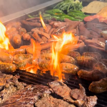 Parrilla al fuego vivo con las llamas sobre los shucos y las salchichas