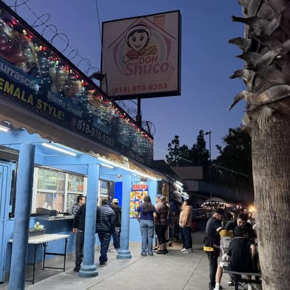 La fila de noche afuera de Don Shuco House bajo el rótulo encendido