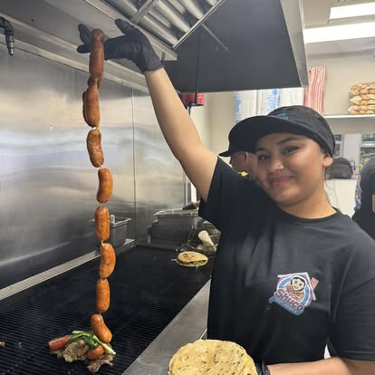 Una cocinera levantando una cadena de longaniza sobre la parrilla